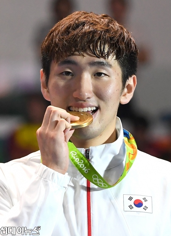 박상영 선수가 목에 걸린 금메달을 환한 미소를 지으며 입에 깨물어보고 있다.
